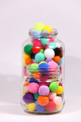 Colorful pompom in glass bottle on white background