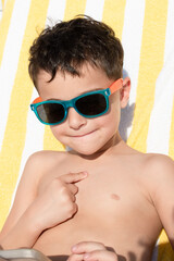 Happy child in sunglasses enjoying summer vacation on a sun lounger. Concept of travel, eye protection from ultraviolet radiation, stylish kids sunglasses. Sunday.