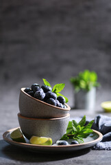 Fresh berries with drops, blueberries with lime, mint in a bowl on a gray background. Summer, freshness, sunshine. Background image, copy space