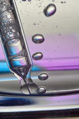 Cosmetic pipette with drops of transparent liquid and a jar, close-up on a colored background.