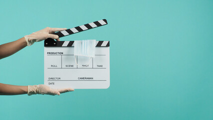 Clapper board or movie Clapperboard or slate with face mask in hand that wear medical gloves on  mint green or Tiffany Blue background.