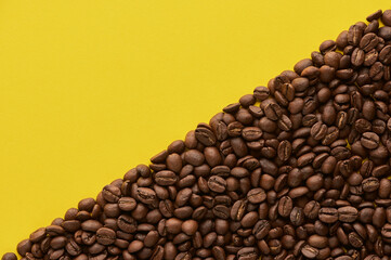 Roasted coffee beans on yellow background with copy space. Close up top view.
