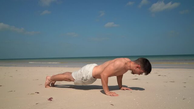 Man does pushups slowly down and fast up on the beach.