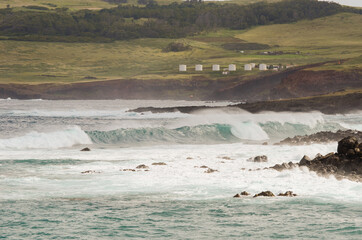 Water tanks of a water treatment plant seen from the rocky coastline and heavy swell of Easter...