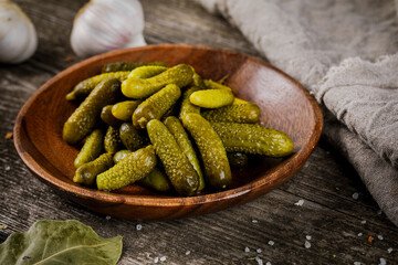 A bowl of pickled gherkins (cucumbers) on a rustic wooden background. Pickles