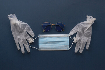 Two medical gloves hold a medical mask on a blue background, sunglasses, top view, copy space.