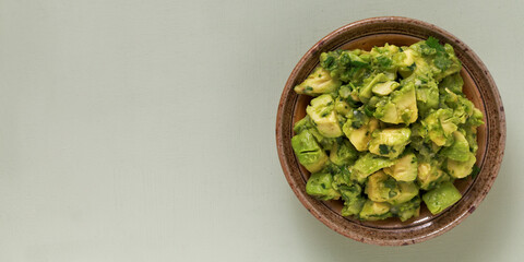 Bowl of freshly made chunky guacamole on bright green background with copy space for text, top view.