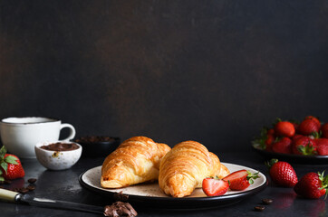 Croissant with chocolate paste and a cup of coffee, strawberries on the kitchen table. ​Traditional snack or breakfast.