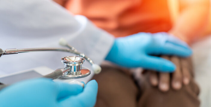 Parkinson and Alzheimer female senior elderly patient with caregiver in hospice care. Doctor hand with stethoscope check up older woman people. Old aging person seeing medical physician in hospital.