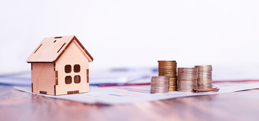 wooden house and pyramids of coins stand on a wooden table