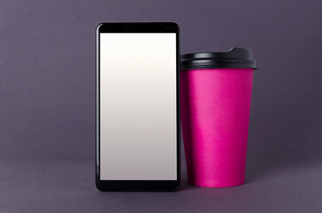 Blank screen of mobile phone and pink paper cup of fresh coffee on the grey surface 