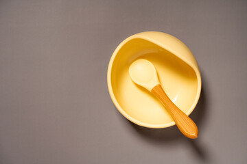 Baby bowl with spoon on grey background. Serving baby food. Flat lay. Copy space