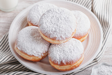 Delicious strawberry jam filled berliner doughnuts on white plate and glass of milk on wooden table...