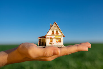 House in hand against spring green field and blue sky