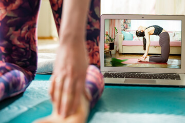 Naklejka premium Beautiful fit woman streaming broadcast video blog about yoga and fitness in living room. Healthy lifestyle and social media. Woman watching video tutorials on laptop and working out at home. 