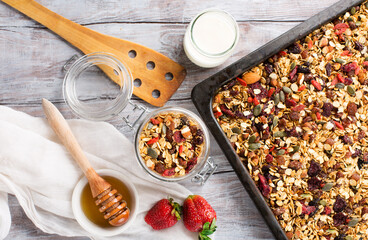 Homemade granola with fresh berries, honey, seeds  on white wooden background.