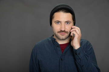 Portrait of young stylish man in casual wear posing with smartphone on isotaled grey background. Concept of communication, call me, talking, be in tought, mobile operator offer package. Copy space