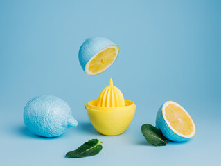 Blue painted lemons with yellow juice squeezer and fresh leaves against pastel blue background. Creative lemonade or natural smoothie concept. Minimal juice bar or healthy vegetarian diet idea.