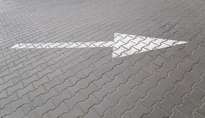 Arrow pointing to the right in white paint in a parking lot made of grey blocks with a geometric pattern