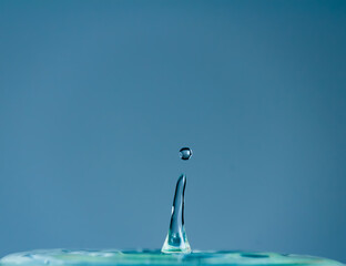 Water droplet falling and splashing on blue background. Macro nature photo
