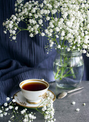 Still life with cup of tea. Simple composition photo with small white flowers and cup of black tea on a table. Beautiful morning picture. 