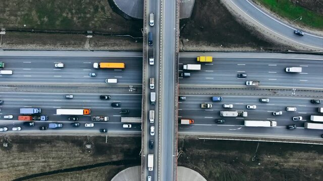 Automobiles and trucks drive along lanes of modern highway with junction and overpass bridge at countryside in spring upper view, timelapse