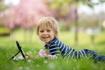 Beautiful child, blond boy, playing on tablet in the park,
