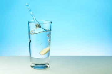 dissolving tablet dissolves in water on colored background. a glass of water and an effervescent vitamin pill. the medicine tablet dissolves in a glass of water