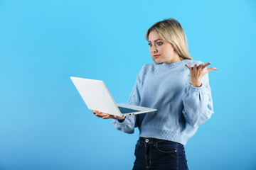confused woman looking through laptop on colored background. young dumbfounded woman using laptop on a blue background.