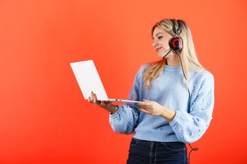 young woman wearing headphones with a microphone holds a laptop on a colored background