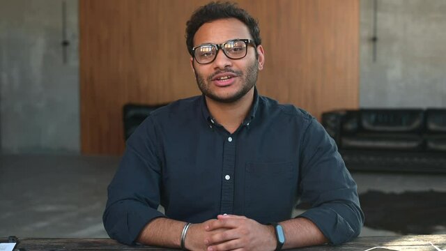 Video chat with multiracial colleague. Smiling hindu guy waving hi, greeting you on online video meeting, video connect with indian teacher, tutor, video call to mixed-race coworker
