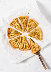 Homemade baked French apple tart green pistachios and vintage cake server on a white baking paper sheet. Flat Lay. Copy space. - obrazy, fototapety, plakaty