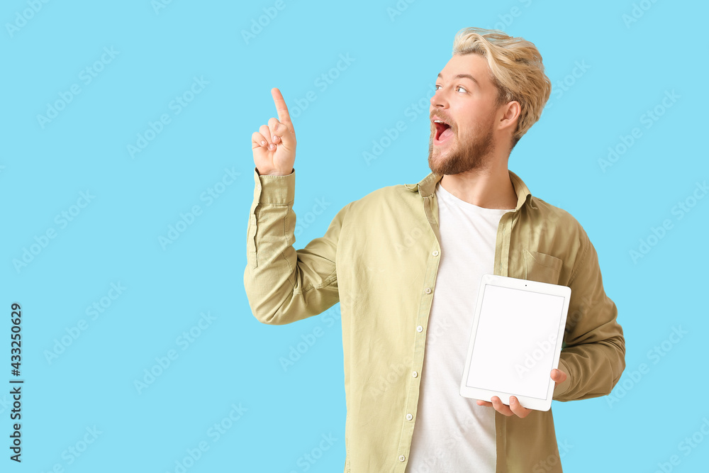 Poster young man with tablet computer pointing at something on color background