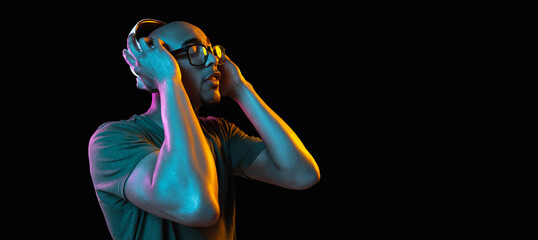 African-american young man's portrait on dark studio background in neon. Concept of human emotions, facial expression, youth, sales, ad.
