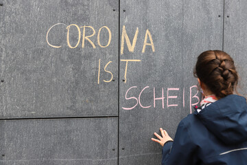 Ein Kind schreibt Corona ist Scheiße auf eine Hauswand