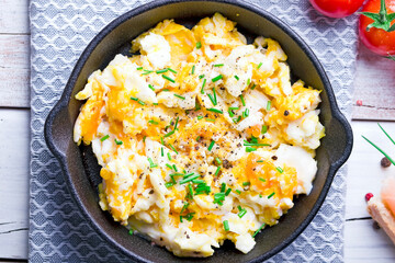 scrambled eggs with chives in a cast iron pan, toasts with salmon and chives, and tomatoes. Healthy breakfasts on an old wooden white table