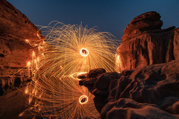 Man wielding rounded burning fire spark from steel wool in rock rapids of grand canyon reflection...