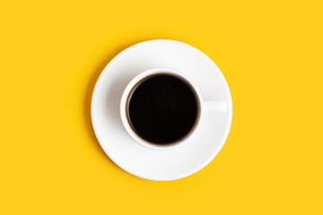 Top view of the white cup of coffee on the yellow background with a free space for text. Getting up early. Wake up with a great mood