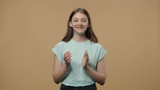 Portrait of charming beauty model clapping her hands with wow happy joy and delight. Young girl in white t-shirt posing on brown studio background. Close up. Slow motion ready 59.94fps.