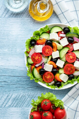 Greek vegetable salad with cherry tomatoes, cucumbers, feta cheese, olives and seasoned with oil. White checkered napkin on a blue wooden table. Top view. Flat lay. Healthy food, a vegetarian diet.