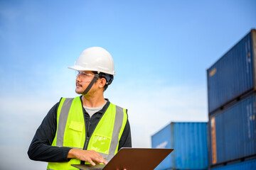 Engineer or a young Asian male foreman Working in the transport of goods using laptops to control the loading of containers at the cargo port for the foreman of the import of export goods.
