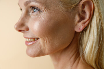 Face closeup of beautiful mature blonde woman smiling away, posing isolated over beige background