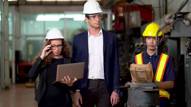 Manager engineer control  Welding robot arms machine discuss with business woman using laptop computer checking monitoring system software of robotics automatic in factory industry. technology