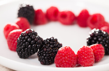 raspberries and blackberries laid out on a white plate in circle