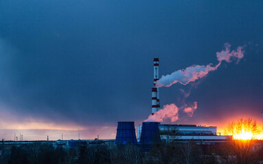 thermal power plant against the background of an evening solar sunset and a blue sky, steam comes from the pipes of the plant. Copy space for text