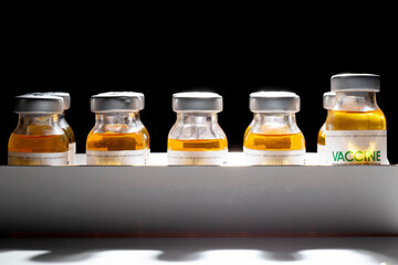 Vials with coronavirus vaccine in packaging on a black background and illuminated by a beam of light. Population vaccination recipe, vaccine research, SARS-Cov-2