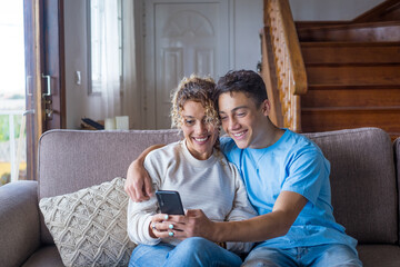 Smiling middle-aged 40s mother rest with grown-up son using smartphone together, happy young man...