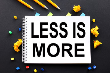 less is more. Text on white paper on black background. and multi-colored buttons and crumpled paper