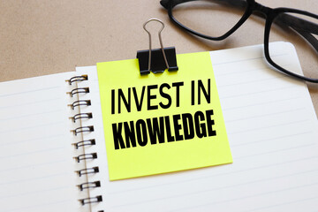 Invest in Knowledge. text on white notepad paper near calendar on wood craft background