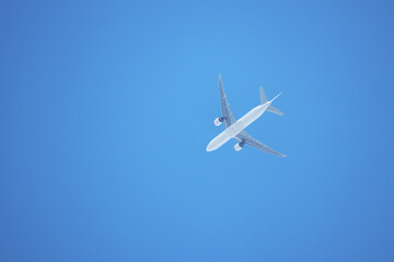 White airplane flying on clear blue sky background, bottom view. Twin-engine commercial plane